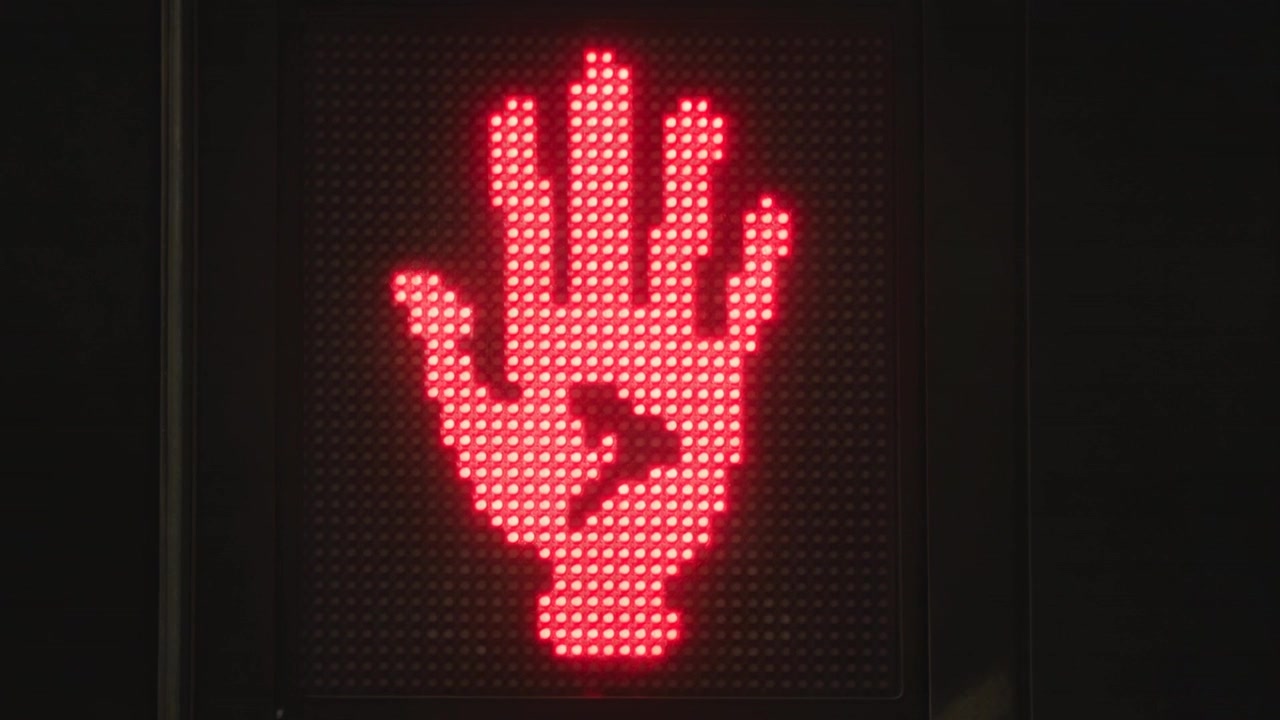 Semáforo LED cambiando de mano roja a peatón blanco en un cruce de calles, con el tiempo de cambio en el panel.