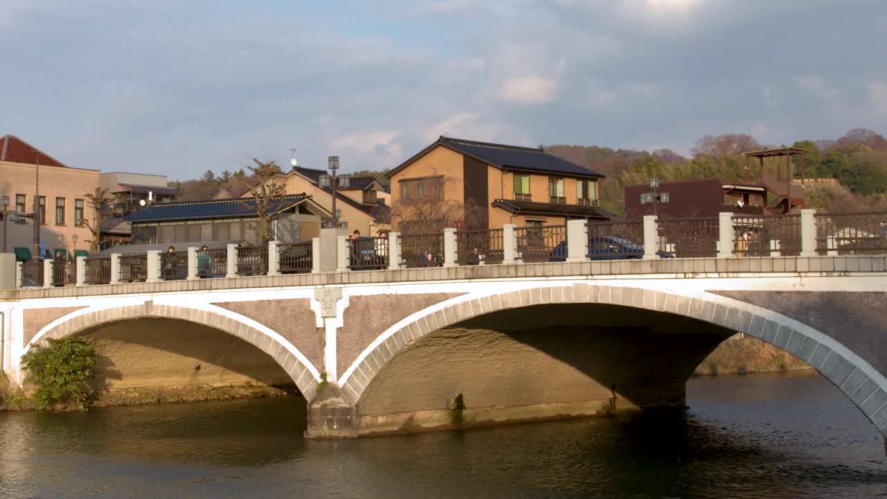Ampia inquadratura fissa di un ponte ad arco storico in pietra che attraversa un fiume sotto cieli nuvolosi.