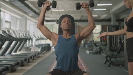 Vista-Frontal-De-Una-Monitora-Caucásica-Y-Un-Atlético-Afroamericano-En-El-Gimnasio.