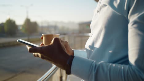 man using phone and drinking coffee outdoors
