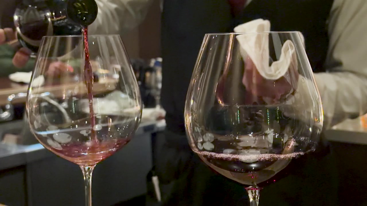 Primo piano di vino rosso che viene versato in un grande bicchiere in un bar poco illuminato.