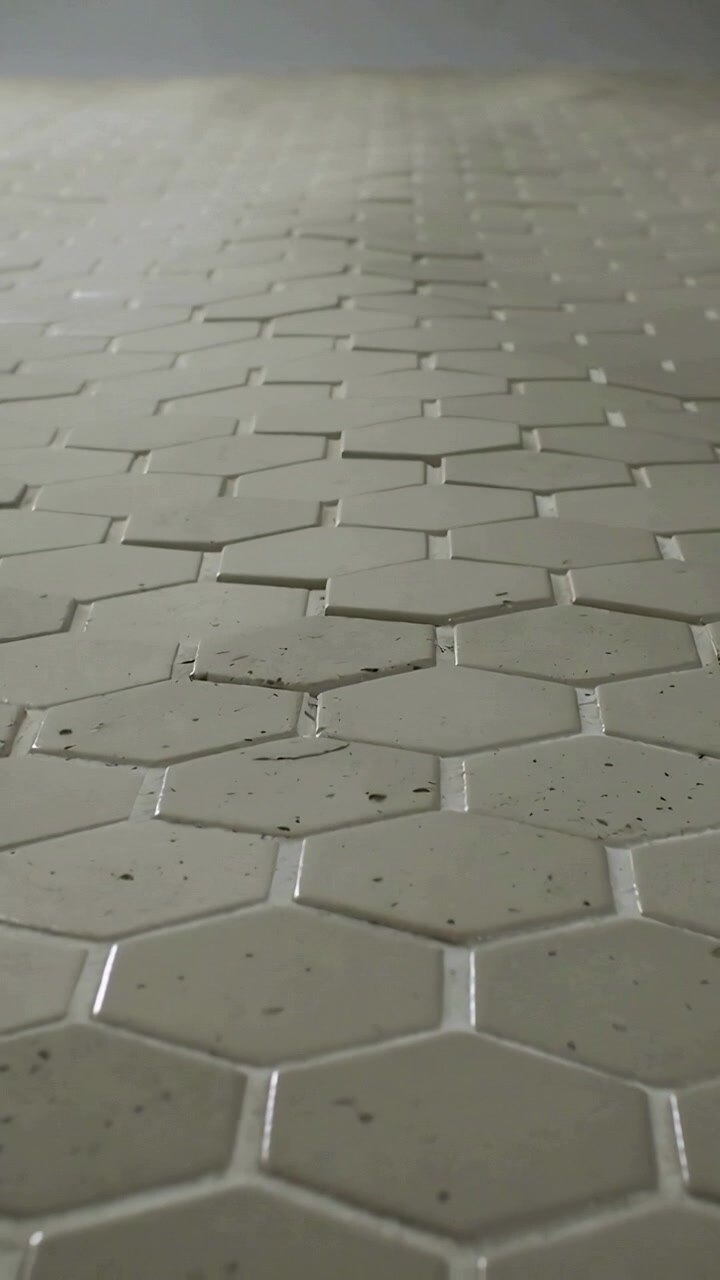 Vertical video: Panning camera starting low, rising along tiles, revealing white hex tiles, grout