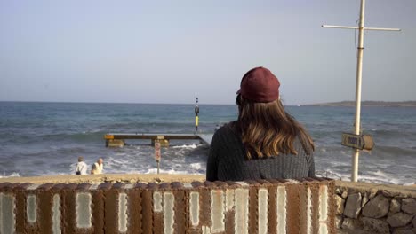 mujer embarazada con sombrero rojo observa las olas del océano en mallorca