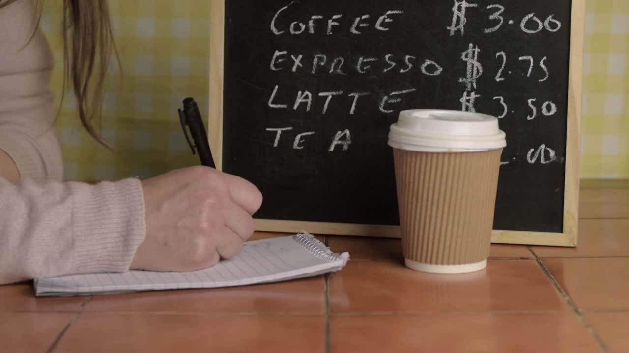 Kvinde, der skriver ved et cafébord med en kaffekop