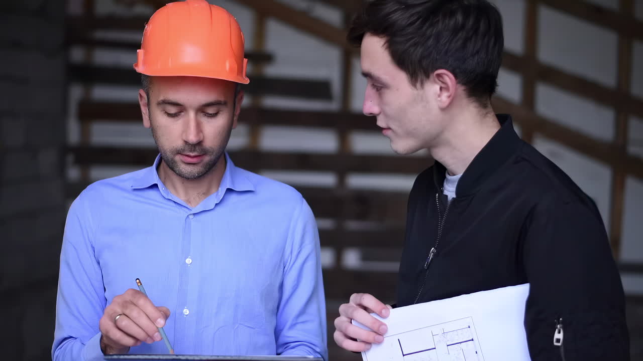 A site manager wearing an orange safety helmet explaining plans to a colleague on a construction site