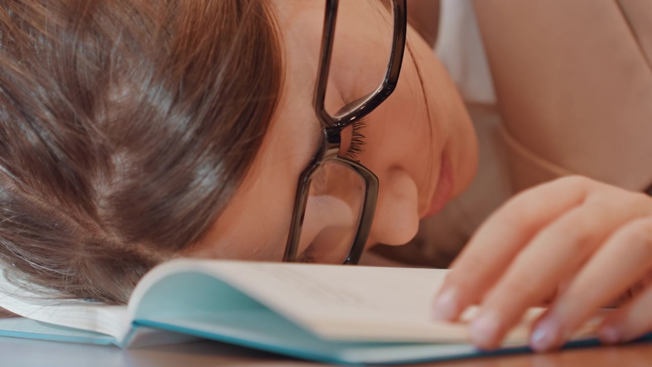 メガネをかけたままくつろぐ学生。夕方遅くの読書中に平和にうたた寝する学生。深夜の図書館での読書に没頭しながら安らかな昼寝を楽しむ穏やかな学生。