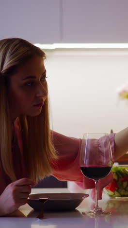 sospechosa mujer rubia agrega polvo venenoso en el vino rojo de los invitados mirando hacia atrás a la cita romántica servida en la cocina en casa en cámara lenta