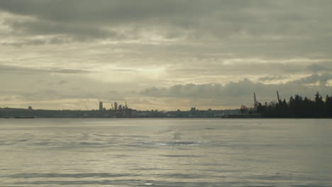 Bird-flying-over-ocean-water-cloudy-sky-and-industrial-cranes-in-background