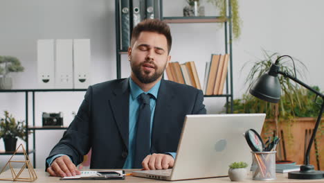 Businessman-working-on-laptop,-meditating,-doing-yoga-breathing-exercise-in-lotus-position-at-office