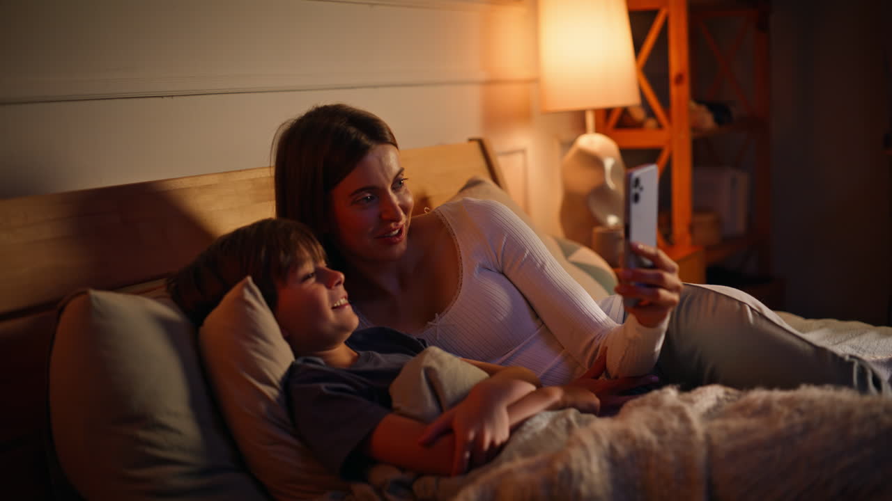 Woman son waving cellphone camera have video call lying cozy evening bed closeup