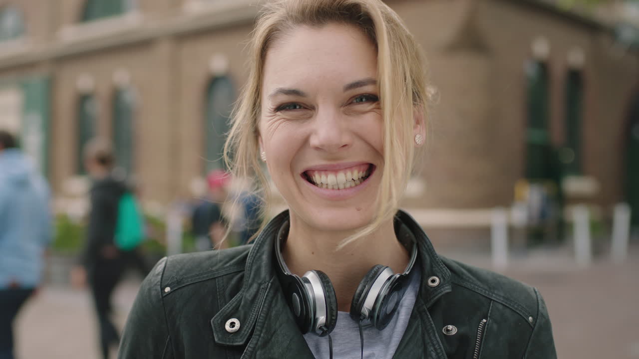 retrato de una mujer rubia independiente sonriendo feliz optimista con auriculares en la acera de la ciudad urbana