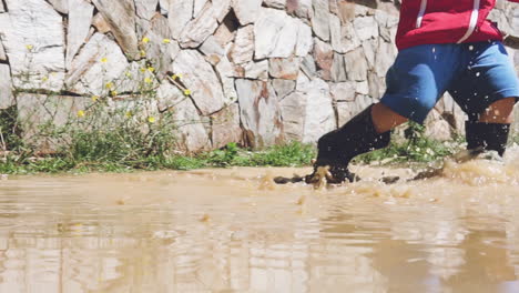 criança brincando em uma poça de lama e correndo na água em câmera lenta depois da chuva