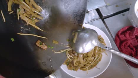 Sirviendo-Fideos-Fritos-Con-Ternera-En-Un-Plato-En-La-Cocina-De-Un-Auténtico-Restaurante-Chino,-De-Cerca