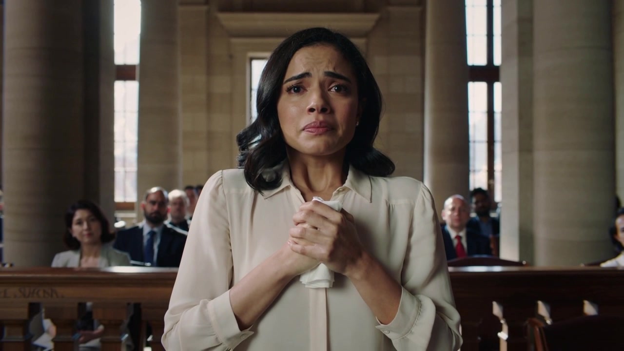Holding tissue, woman pleading and answering court questions at courtroom railing, beige top