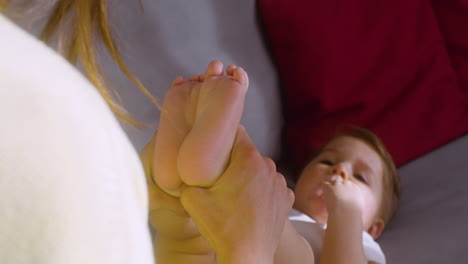 close up view of a smiling baby lying on the sofa at home while his mother playing with him and holding his legs