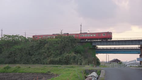 red countryside local train crossing bridge in mikuriya, tottori japan