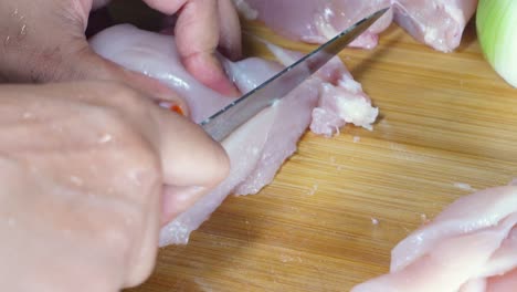 close-up of a person cutting chicken breast on a wooden board