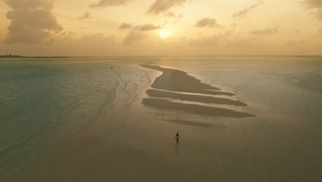 Woman-in-white-bathing-suit-walking-on-tropical-sandbank-during-sunrise