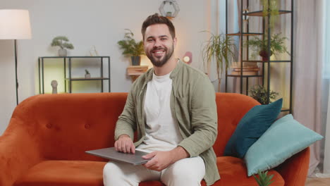 happy caucasian man sitting on couch closing laptop after finishing work in living room at home