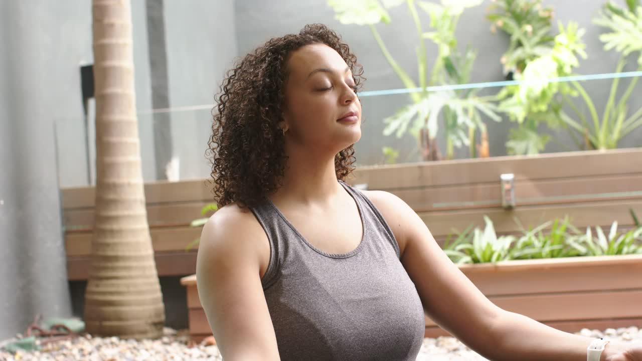 African American woman having palms up, sitting on patio in gray tank with tracker, calming