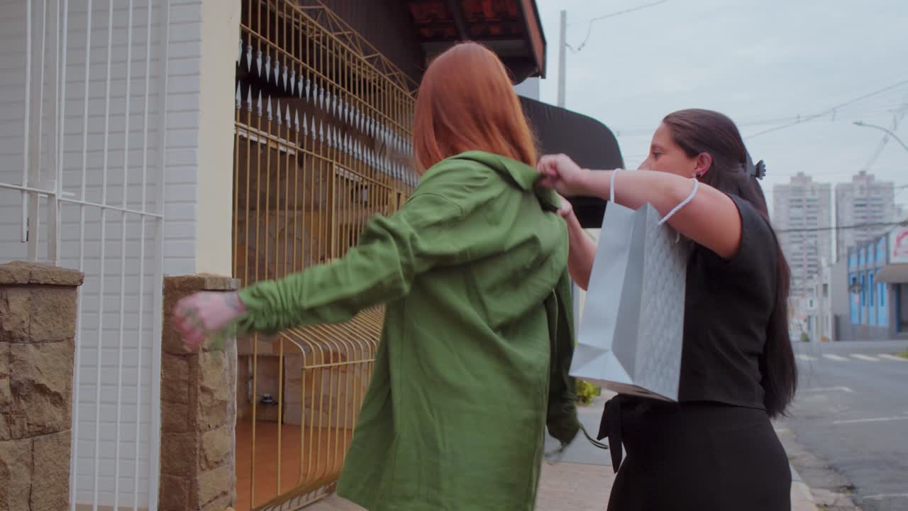 Two women exchanging a green garment from a shopping bag on a street