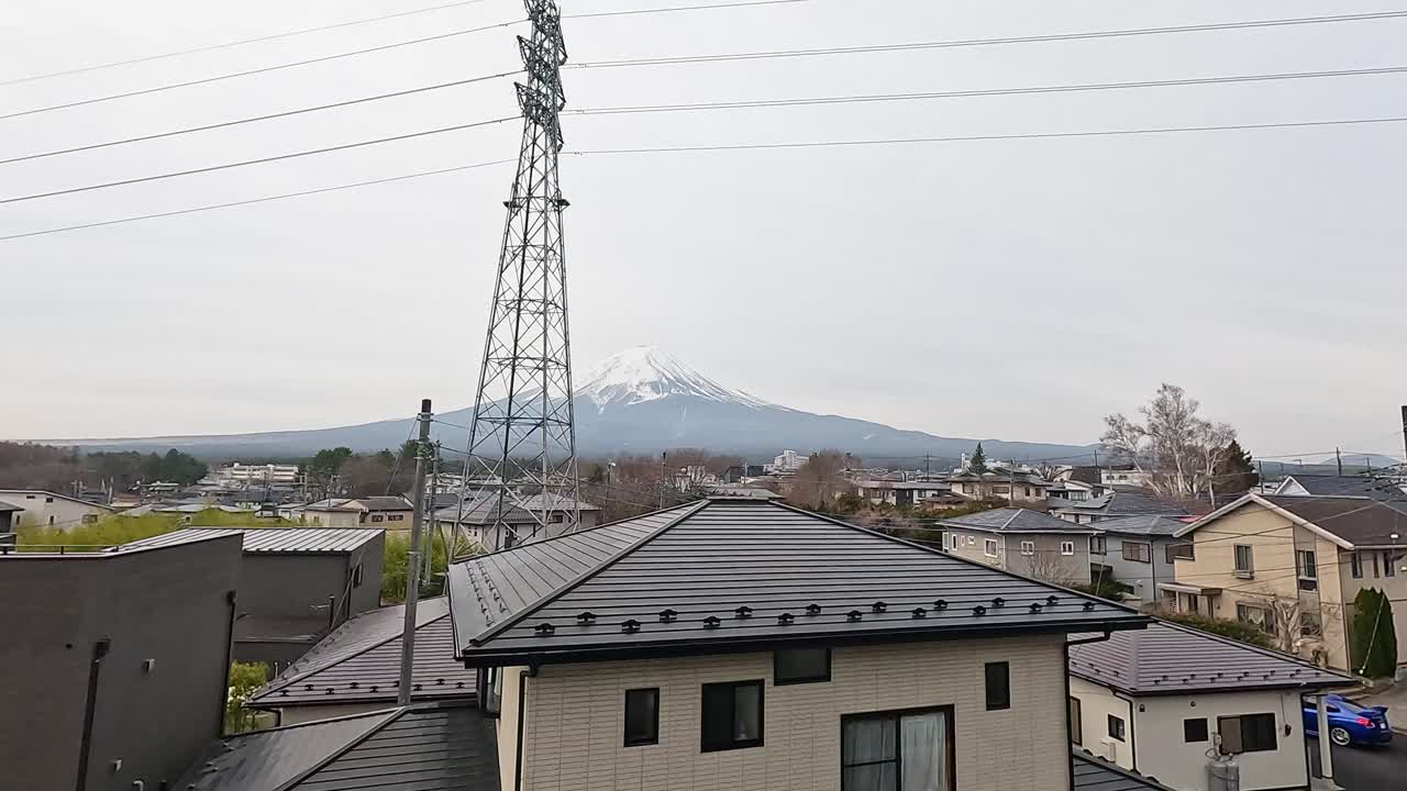 A serene view of Mount Fuji with rooftops and power lines in Kawaguchiko, Japan. Overcast lighting creates a calm atmosphere
