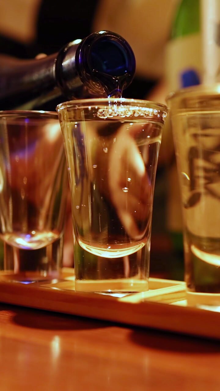 Sake giapponese trasparente si versa da una bottiglia blu in un bicchiere al rallentatore.