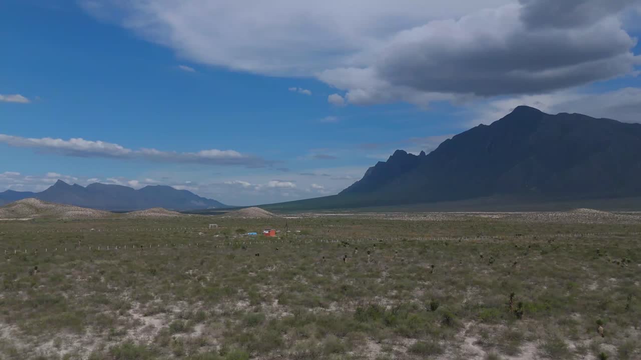 Vast desert semi-desert landscape with mountains in the background and a small farm in the distance and cacti around 4k 60 fps
