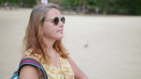 Woman-in-sunglasses-spending-the-weekend-outdoors,-sitting-and-looking-around-in-the-park---close-up