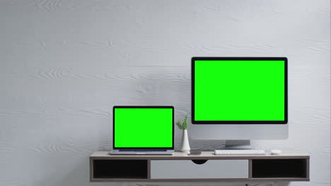 monitor montado en la pared y portátil con pantallas verdes y escritorio contra pared de textura blanca, cámara lenta