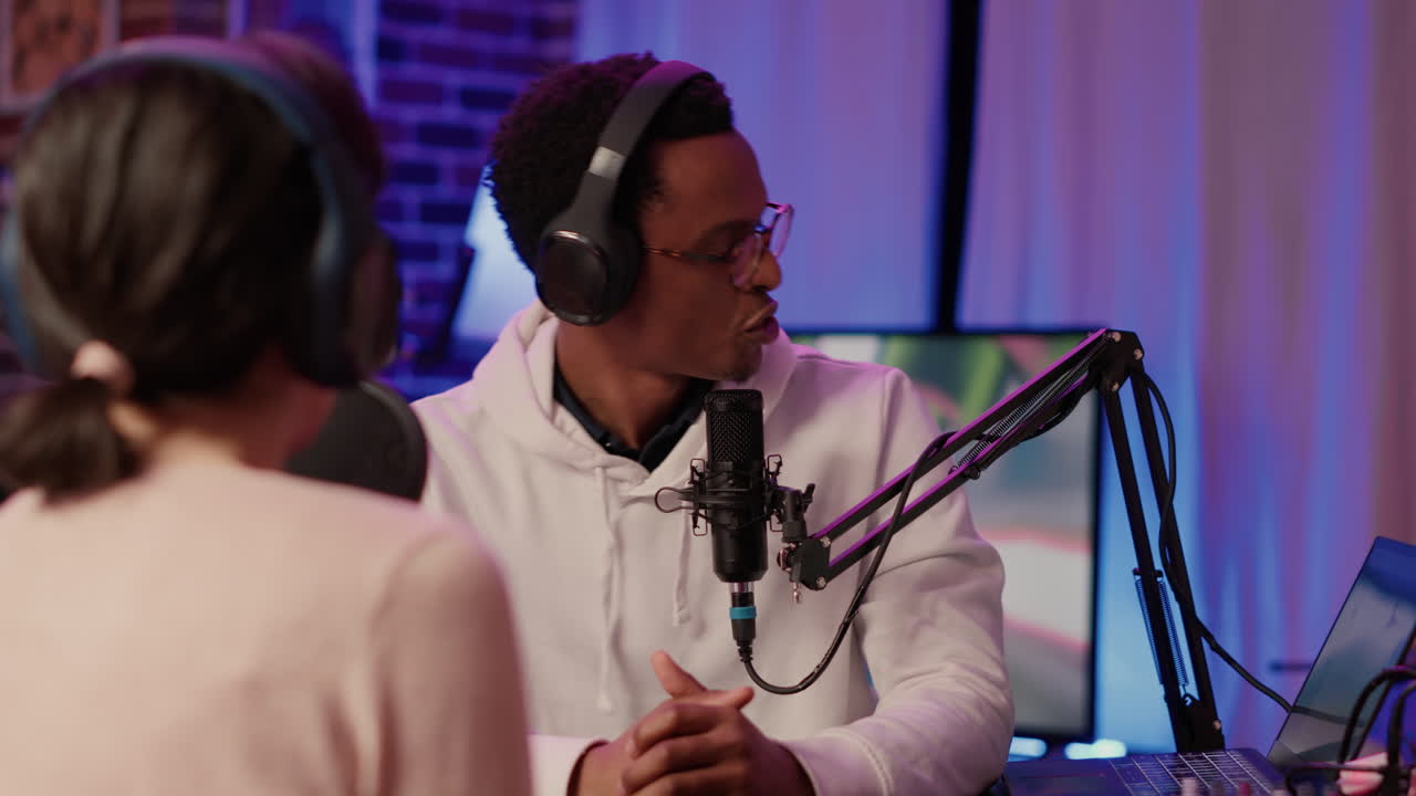 Internet podcaster reading question from laptop screen talking using microphone to influencer guest