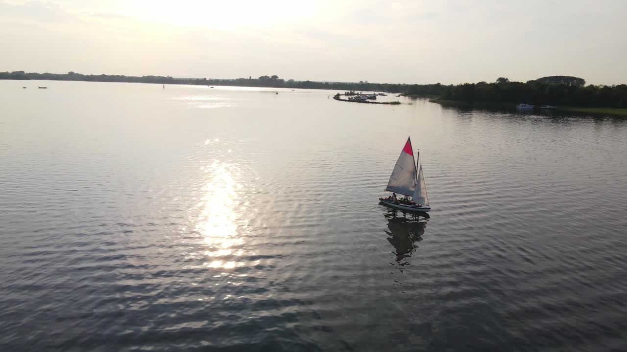Una vista aerea di una barca a vela solitaria che scivola con grazia sulle acque serene del lago Wijde Blik, Paesi Bassi, durante un tramonto calmo, creando una scena pacifica e pittoresca.