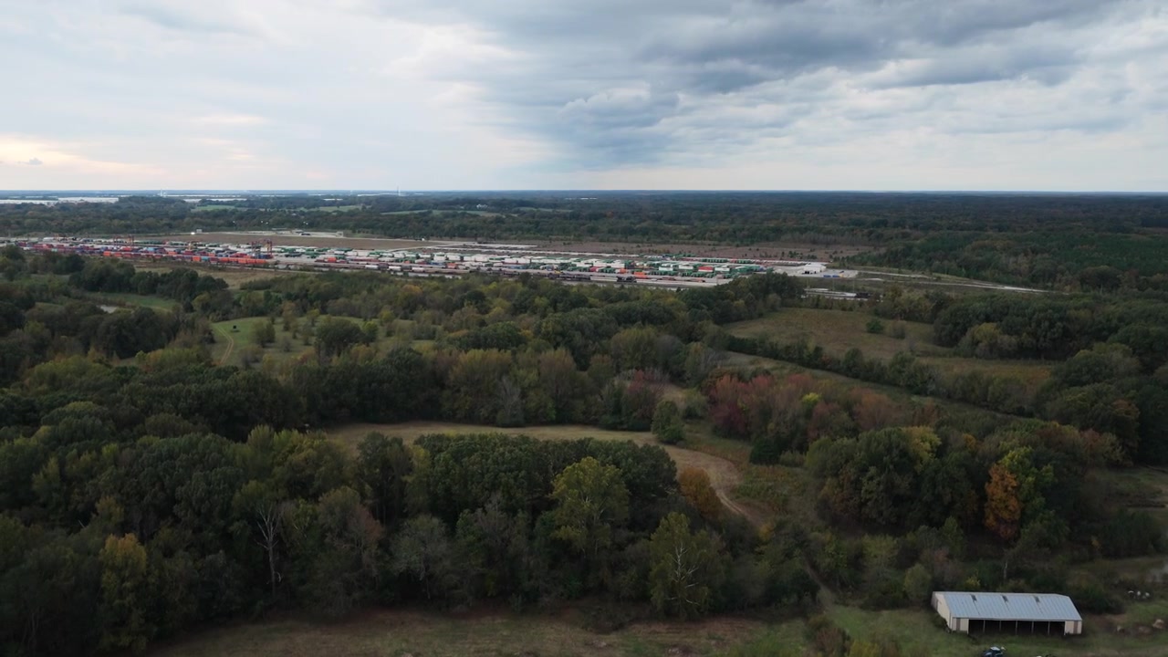 Wide aerial pan left of rural farmland and woodland near logistics hub in Rossville, drone