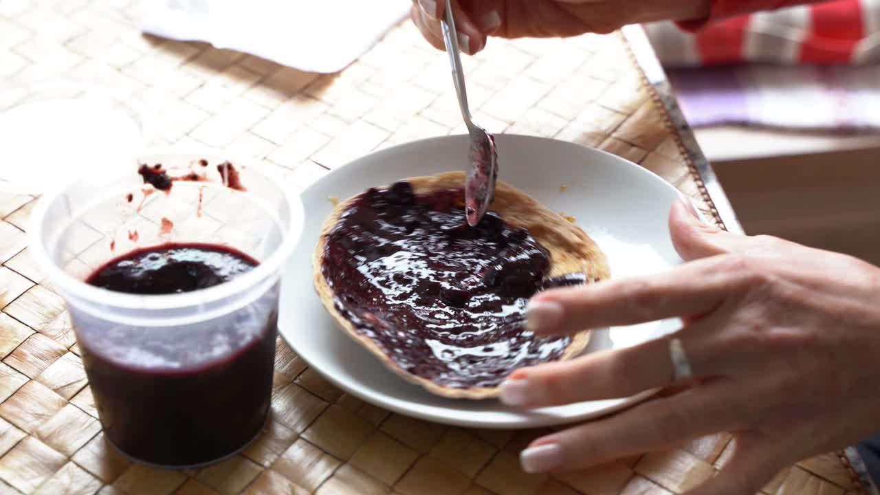 Hand of woman spreading blackberry jam on pita bread for breakfast
