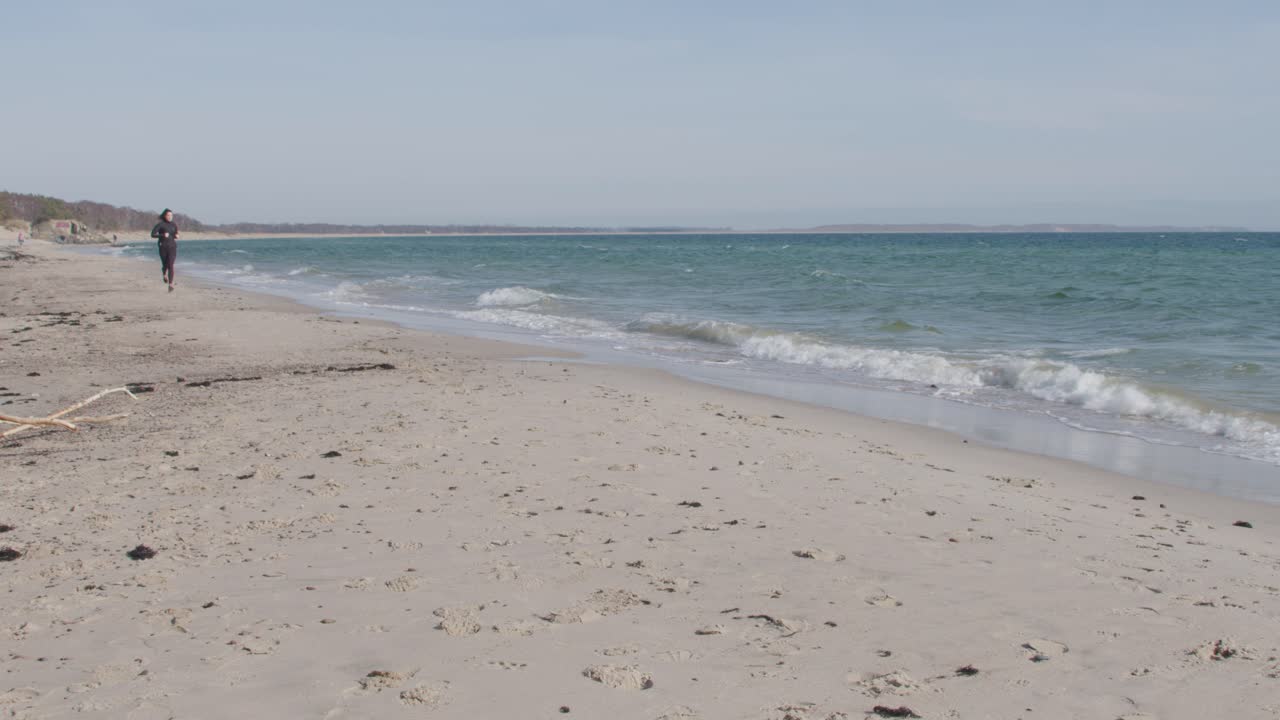 Young fitness athlete jogging on the beach along the waterline towards the wide angle camera