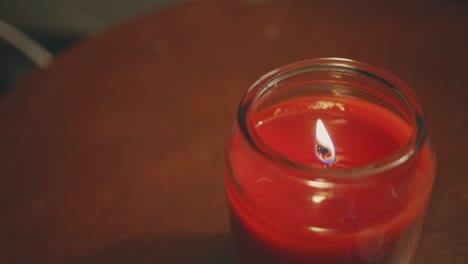 burning candle on a glass jar placed on a wooden table - close up