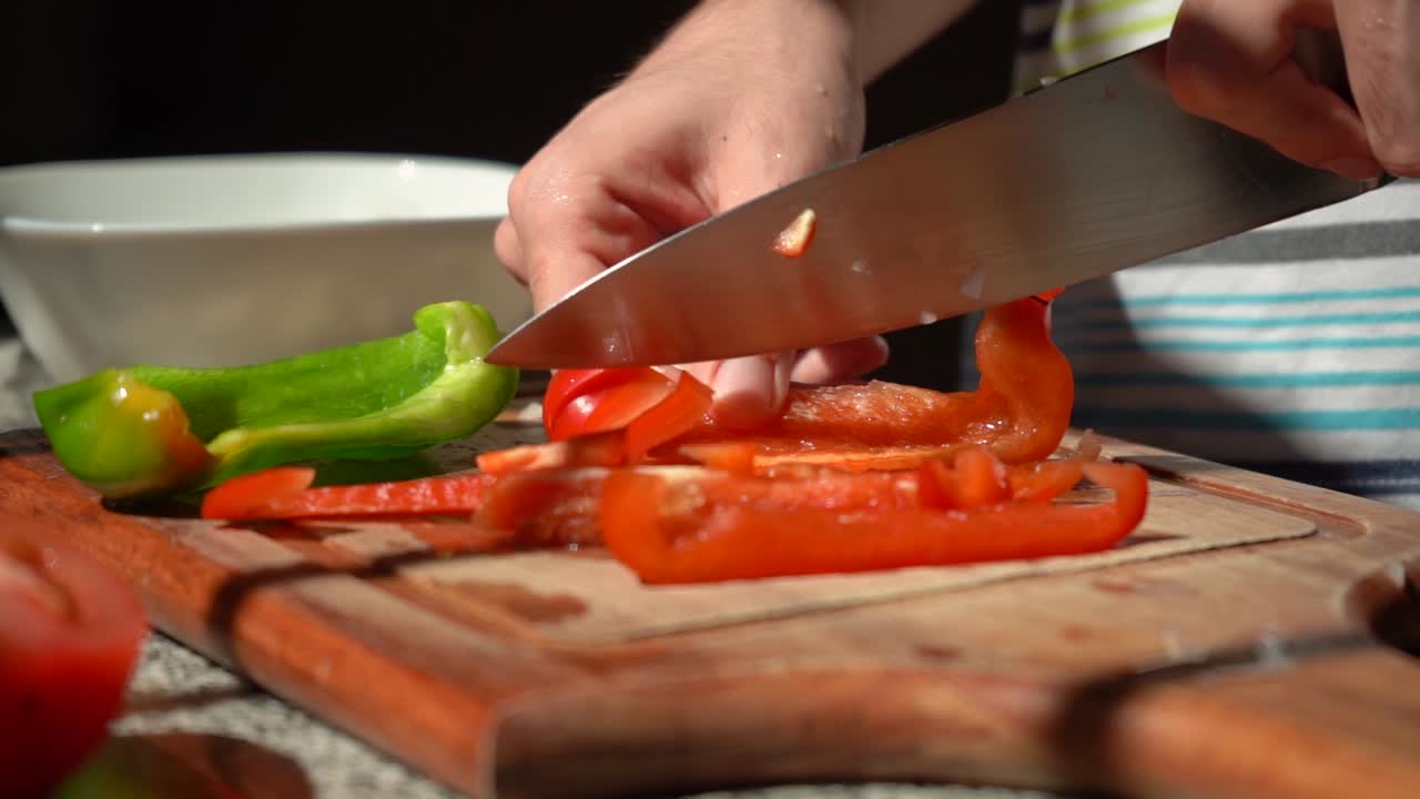 persona cortando pimiento rojo con un cuchillo sobre una tabla de cortar en la cocina.