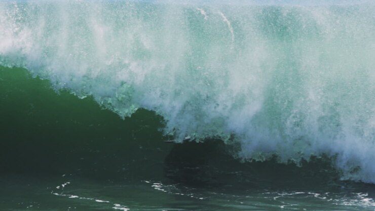 Surfer disappears into smooth emerald barrel as sunlight glows through wave surface