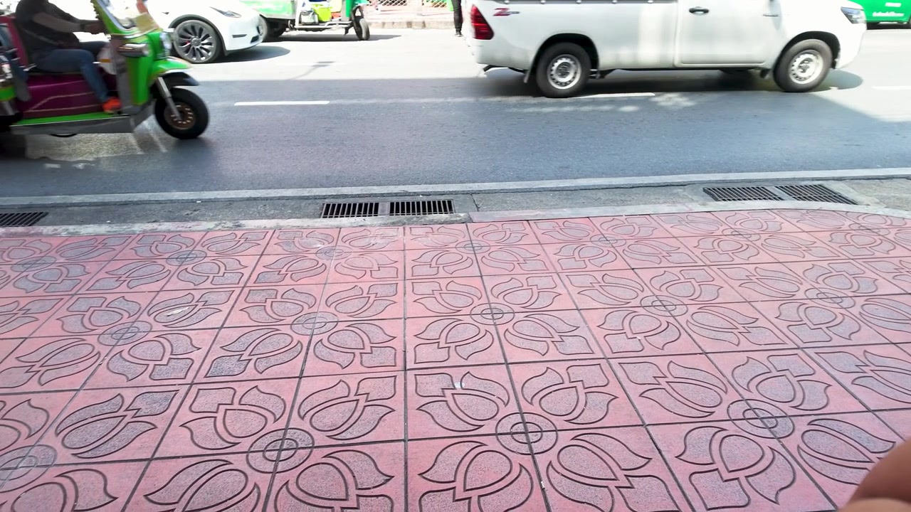Static shot of decorative pink lotus tiles on a sidewalk with passing city traffic.