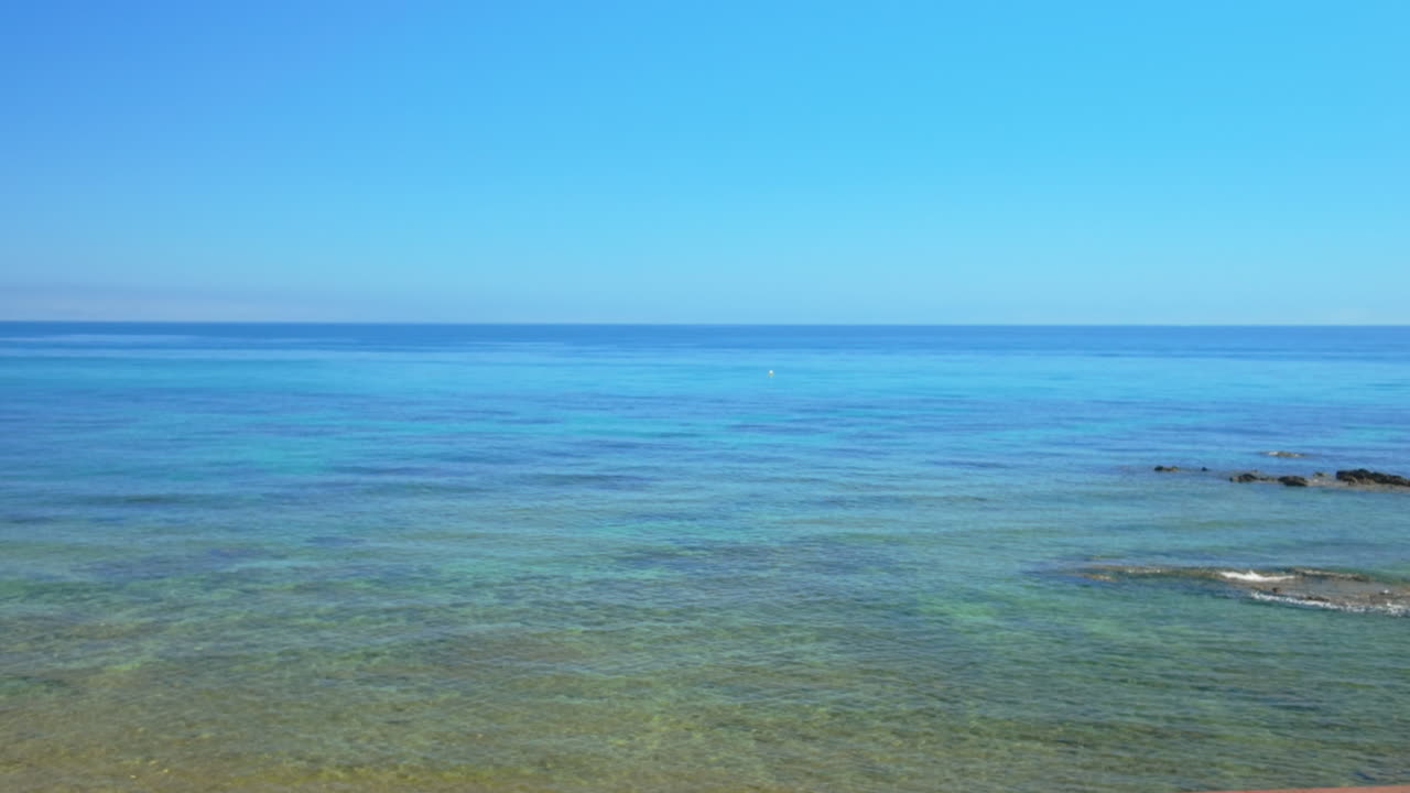 Wooden stairs leading to the turquoise waters of the Mediterranean Sea in Marbella, Spain, under a clear blue sky