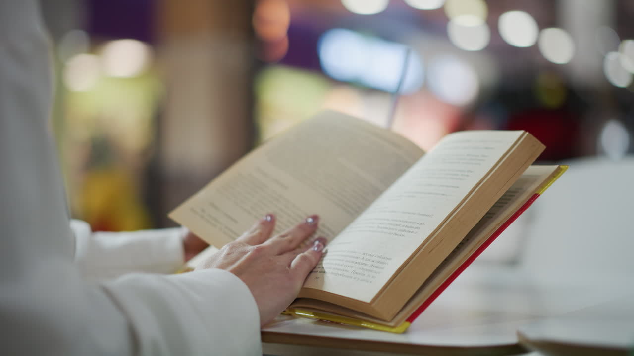 primer plano de manos volviendo las páginas de un libro abierto con un fondo borroso con luces suaves, creando una escena tranquila y reflexiva