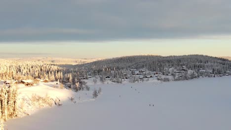 Aerial-view-of-winter-resort-with-frozen-lake-and-skiers-in-Norway