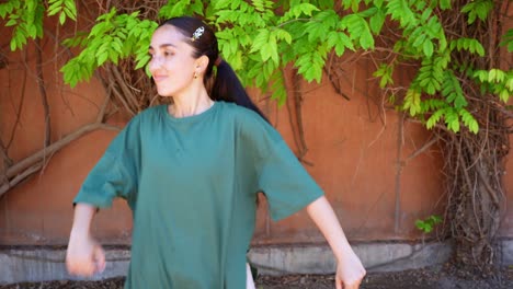 woman in green shirt posing in front of a wall with foliage