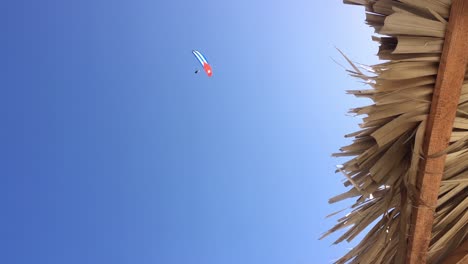 straw beach umbrella, blue sky and peson on paraglide with cuban flag wing