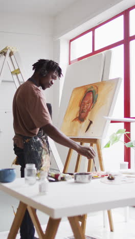 african american artist paints in studio, headphones on, vertical shot