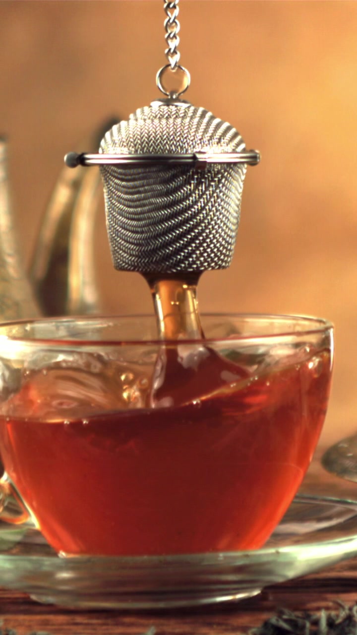 Rallentatore di un infusore da tè che gocciola in una tazza di vetro di tè caldo