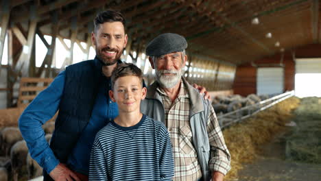 grandfather, father and grandson farmers looking at camera in a stable with sheep flock