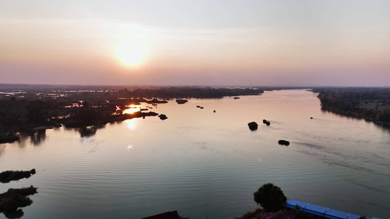 A peaceful sunset unfolds over the Mekong River at Don Det, Laos, with golden reflections on the calm water, scattered islets, and a quiet riverside village creating a serene evening atmosphere