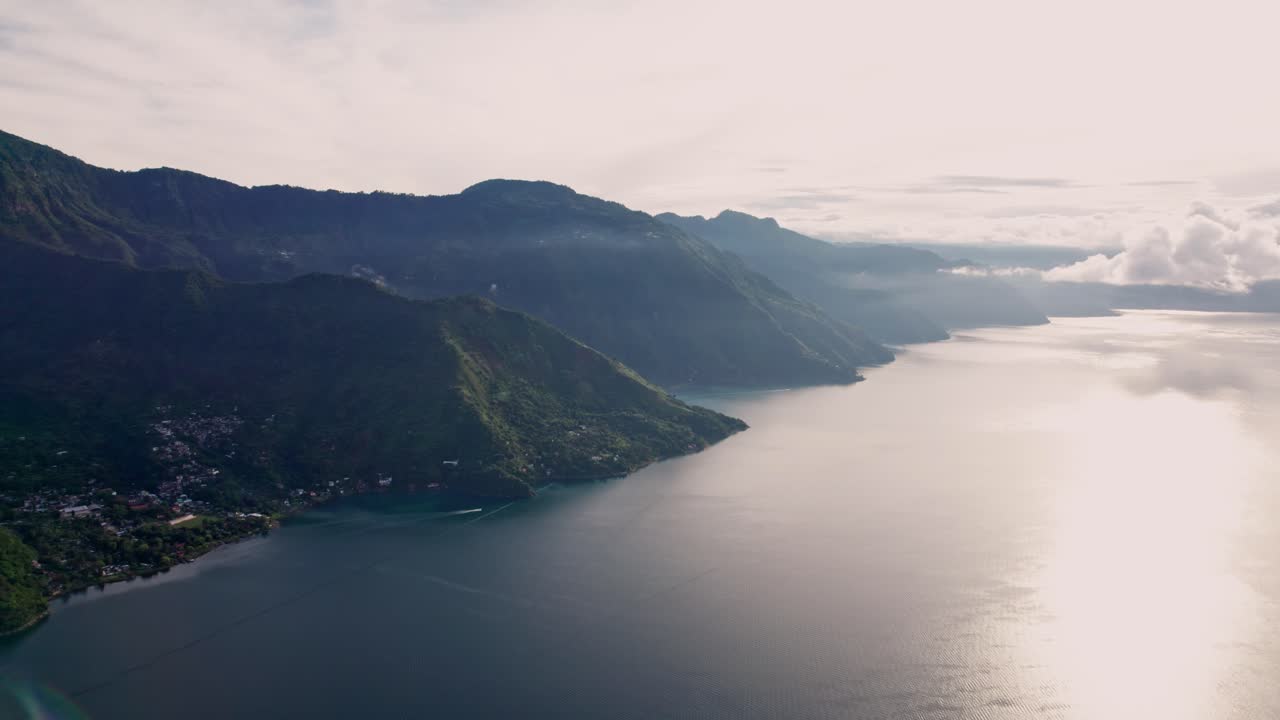 A breathtaking high-altitude drone shot captures a long pier extending into the glassy, reflective waters of Lake Atitlán at sunrise