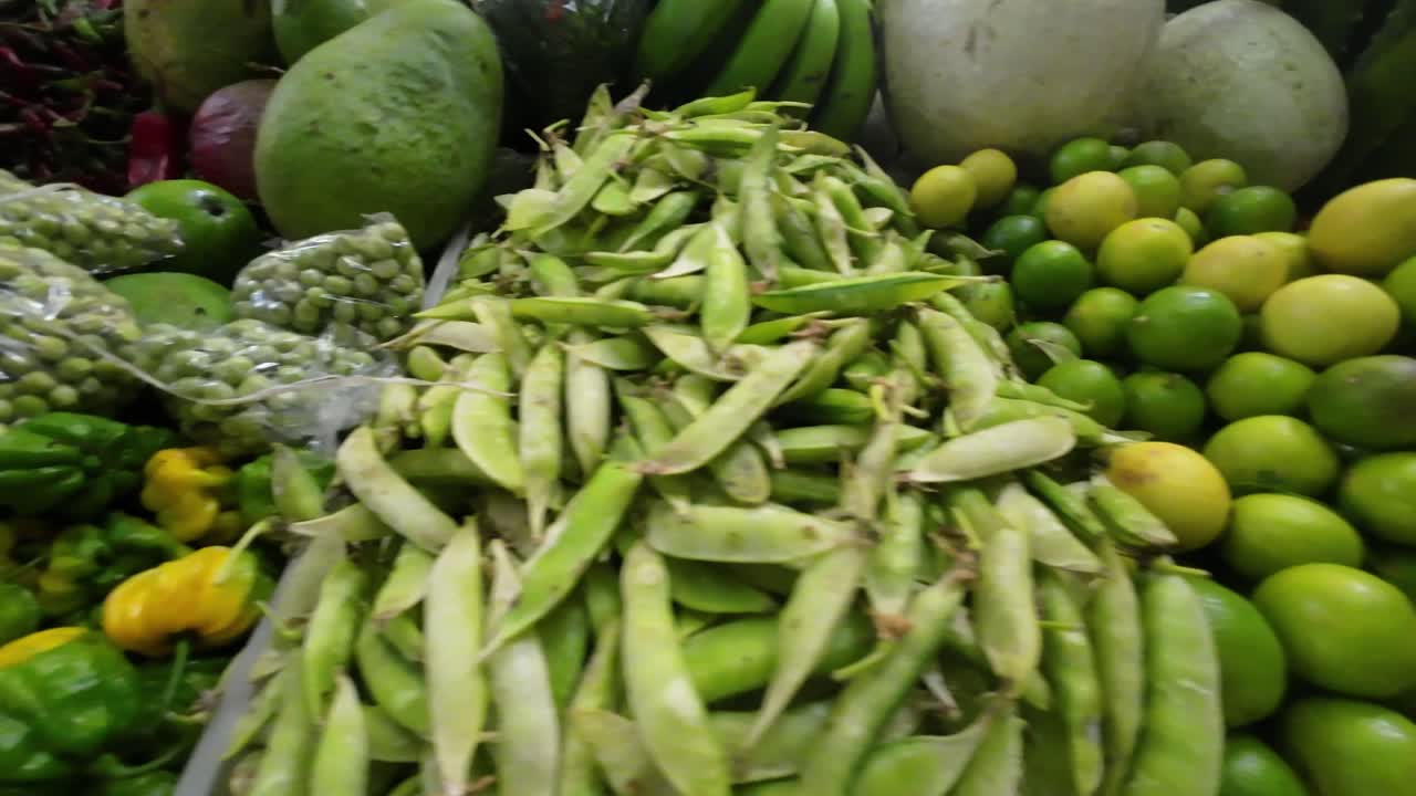 Side pan across limes, mangoes, and hot peppers on a colorful market stall in Caracas, Venezuela.